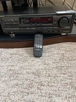 Front view of the Technics stereo receiver and the remote control placed in front on the carpet.