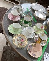Top down photo of 10 assorted vintage teacups and saucers on glass table showing varied colors and floral designs