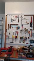 Wide shot of pegboard with various hand tools including pliers, wrenches, screwdrivers, scissors, and saws organized on hooks.