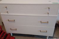Front view showing white dresser with three drawers and metal toned pulls and knobs.