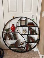 Full view of the round wall hanging showing multiple shelving sections with decorative books, clock, and vases.