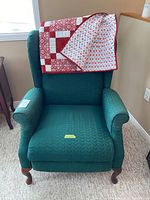 Green upholstered wing-backed reclining chair with lap quilt draped over the back.