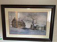Full view of framed print showing winter limestone house scene with snow and bare trees under dark wood frame and matting.
