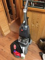 Full view of Hoover Turbo Scrub carpet cleaner upright, with bag, instruction manual, and two bottles of cleaning solution in front.