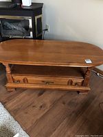 Oval wooden coffee table front view showing drawer, lower shelf, and turned legs.