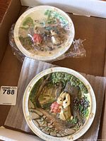Two round ceramic decorative plates with Peter Rabbit characters, one musical, placed in a cardboard box with padding.
