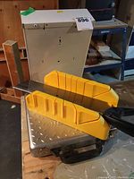 Hand saw with black handle in yellow plastic miter box on a workbench