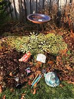 Photo of entire garden lot on soil and grass showing birdbath, metal spiral flowers, red bird figurine, garden stakes, and ornaments.