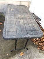 Top and angled view of the black plastic folding table showing textured grid surface with visible wear.