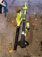 Overview of Ryobi weed eater with detachable handle and cutting head, leaf blower, and screwdriver on garage floor.