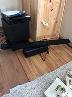 Sony HDMI box, subwoofer, sound bar, and remote control on wood floor against light wood panel wall next to a cabinet.