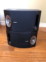 Front view showing two black Bose speakers stacked, fabric grills and silver cones visible, with wear and tear.