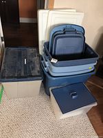 Five plastic totes and storage boxes stacked in a room showing the various lids and sizes