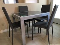 Overall view of the grey metal and glass table with four padded chairs.