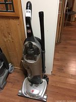 Front and side view of Hoover vacuum cleaner showing overall shape, hose, and handle with clear dust container.