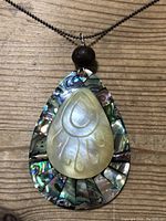 Close-up of pendant necklace showing mother of pearl carved teardrop on abalone inlaid teardrop backing, wooden bead, and metal ball chain.
