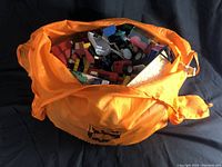 Orange bag filled with assorted LEGO pieces visible inside, showing various colors and types of bricks and parts.