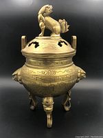 Front view of the brass censer showing the lion figurine on the lid, ventilation cut-outs, and detailed engravings on the body and legs.