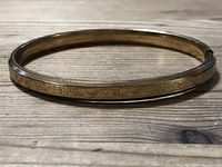 Full view of the oval-shaped gold-tone bracelet showing overall shape and wear.