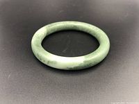 Front angled view showing the smooth, rounded jade bangle and color variations in the stone.