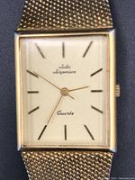 Close up front view of the Jules Jurgensen watch face showing the rectangular shape, gold-tone edges, and off-white dial with gold-tone linear hour markers and hands. The watch face reads 'Jules Jurgensen' and 'Quartz'.