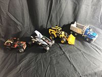 Four LEGO vehicles arranged on a black cloth background: off-road vehicle, futuristic car, bulldozer, dump truck