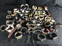 Full overview of large watch lot against black fabric background showing variety of styles including bangle, cuff, leather and metal strap watches