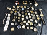 Wide shot displaying approximately 55 assorted vintage wristwatches in various conditions, some with bands, others without, laid out on black cloth.