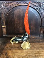 Front angle showing the tall red comb, black and green body, and golden swirled base of the Murano glass rooster figurine placed on a wooden surface.