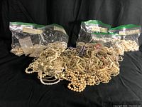 Pile of multiple pearl necklaces on black background with several zip-top bags behind