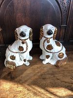 Front view of both Staffordshire dog figurines, showing white porcelain with gold accents and chain collars.