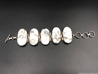 Six large oval abalone shell panels with silver mounting and toggle clasp, laid flat on black background.