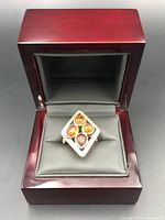 Front view of the vintage silver ring with four amber stones set in a square design inside a grey cushion in a wooden ring box with a dark reddish finish.