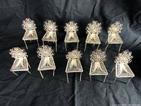 Top-down group photograph of all 11 silver miniature chairs arranged in rows on a black cloth.
