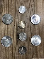 Top view of eight assorted vintage silver quarters and dimes laid out on wooden surface showing front sides with various motifs and wear.