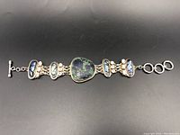 Full bracelet view on black background showing silver, abalone, green stone and toggle clasp.