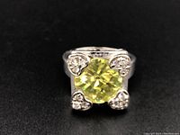 Front view of silver ring with round yellow gemstone held by heart-shaped prongs with clear stones