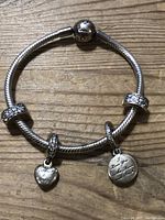 Full view of the silver Pandora bracelet with visible two charms and two rondelle charms on wooden surface.