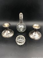 Full set displayed showing cut crystal bottle with silver neck and stopper, two sterling silver candle holders, and small crystal dish against black background.