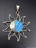 Front view of sterling silver sun-shaped pendant with a moon face and an opal inlay showing blue and green colors.
