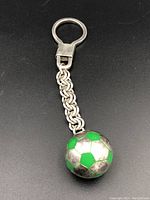 Front view of a sterling silver keychain with a soccer ball pendant featuring green enamel panels and chain link attached to a keyring, on a black background.