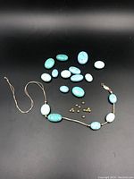 Necklace with turquoise stones strung on beige cord, separated loose turquoise stones and gold beads on black background.