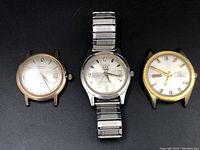 Three Benrus wristwatches side by side showing different dial designs and metal or gold-tone cases, one with metal expansion bracelet.