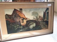Front view of framed and matted hand colored etching showing rustic village bridge scene.