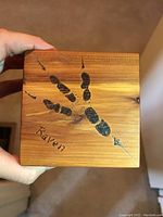 Top view of red cedar box lid featuring black raven handprint and handwritten word 'Raven'