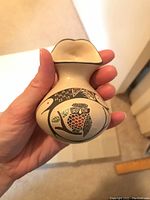 Photo showing owl shaped pottery piece with detailed black and rust colored paint designs and hand-held for scale.