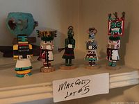 Five miniature kachina dolls displayed on shelf with label.