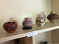 Four signed Native American pottery pieces displayed on a shelf showing varied shapes and traditional painted designs.