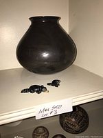 Full view of the black polished pottery pot and two black beaver fetish figurines on a shelf with a sign indicating Max Sold Lot #3