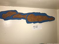 Full view of the wood carving mounted on a wall showing the elongated shape and blue border with carved seal and salmon figures.